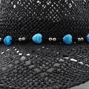 Detailed macro view of black straw hat weave with blue heart bead and metallic accents