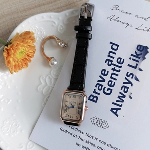 Close-up of retro rectangular rose gold watch with black leather strap on a ceramic plate