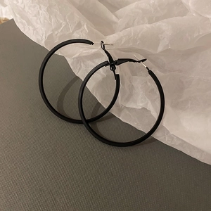 Detail view of matte black geometric hoop earrings on textured minimalist background
