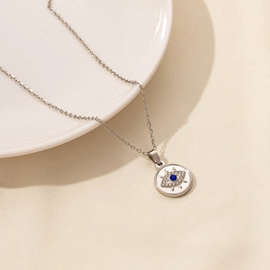Detailed shot of silver evil eye pendant with blue crystal on a white ceramic plate