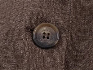 Vue détaillée d'un bouton marron à quatre trous sur le tissu d'un blazer texturé foncé