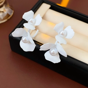 Macro detail of white floral earrings with pearls displayed in a premium black jewelry box