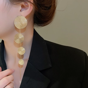 Model wearing gold long tassel earrings with four textured circular metal discs in tiered style