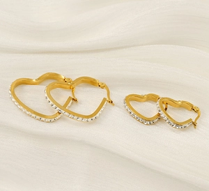 Macro detail of gold-plated heart earrings with rhinestones on white silk