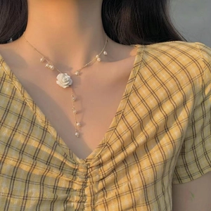 Elegant gold Y-shaped necklace with white rose pendant and pearls worn by a model