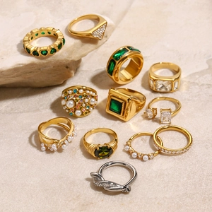 Flat lay of gold and silver rings with emerald gems and pearls on a sandstone surface