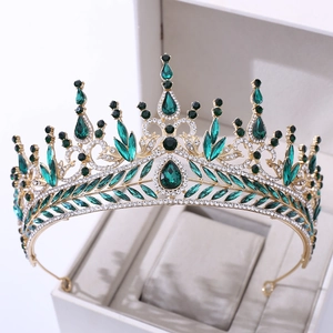 Detailed close-up of a gold baroque crown with emerald green crystals and rhinestones