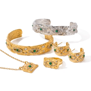 Golden Evil Eye jewelry set featuring textured metal, green gems and crystals on white background
