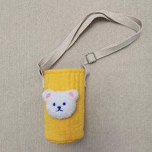 Close-up of a yellow quilted fabric water bottle bag with a plush bear patch and strap