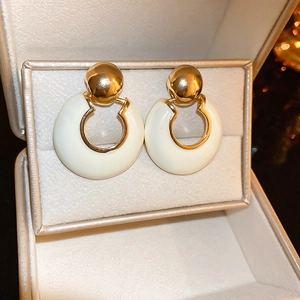Detailed close-up of retro gold-plated hoop earrings with white enamel charms in a gift box