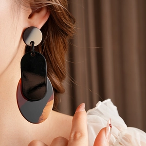 Close-up of oversized tortoiseshell acrylic drop earrings worn by a model