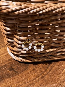 Detail of 925 silver pearl stud earrings on a brown woven basket over a wood surface
