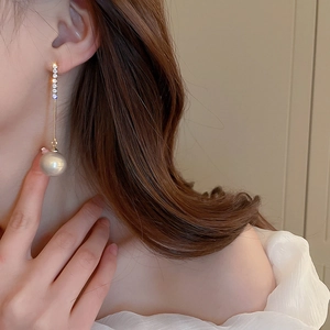 Close-up of dangling pearl tassel earrings with rhinestones on a female model