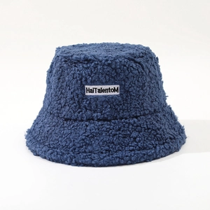 Detail of navy blue fuzzy bucket hat featuring embroidered letter patch on lamb wool texture