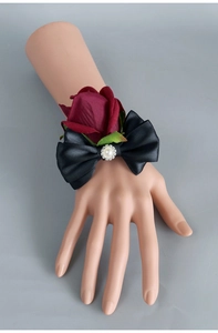 Detail of dark red silk rose wrist corsage with black satin bow and pearl accents
