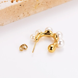 Gold plated C-shaped earrings with inlaid pearls on white minimalist stone background