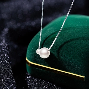 Detail of white double faux pearls on a silver box chain over a dark green velvet box