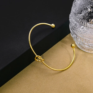 Detailed close-up of golden knot open bracelet with metal balls on grainy dark background