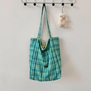 Detail of green plaid canvas tote bag hanging on a hook with a cute plush sheep charm