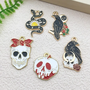 Detail of five Gothic enamel charms featuring skull, black snake, and crow on beige background