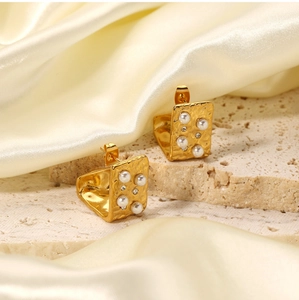 Detail of 18K gold stainless steel earrings with pearls and crystals on beige stone
