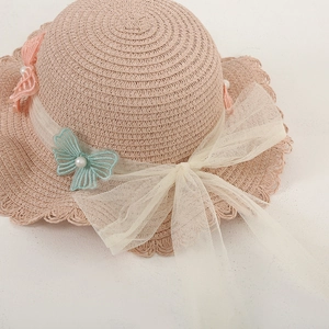 Close-up of pink beige woven straw hat with lace bow and pearl butterfly detail