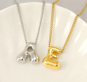 Macro shot of 3D puff letter A and E pendants in gold and silver finish on a shell tray