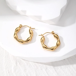 Close-up of golden irregular wavy hoop earrings on a white geometric stone display