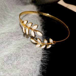 Detailed close-up of golden leaf-shaped open cuff bracelet with white enamel inlay