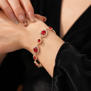 Dettaglio di un bracciale a cuore vintage dorato con strass rossi al polso