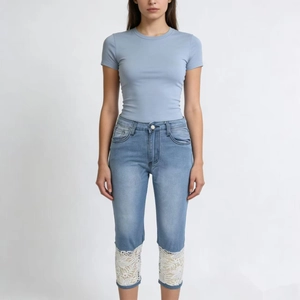Detail of white lace patchwork on the hem of light blue denim cropped pants