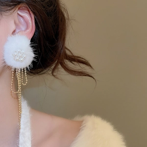 Close-up of white fur pompom flower earrings with long gold beaded chain tassels