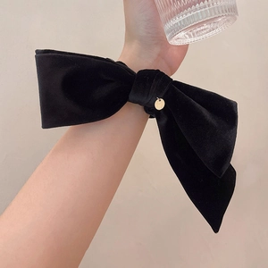 Close-up of black velvet bow scrunchie featuring a delicate circular metal charm
