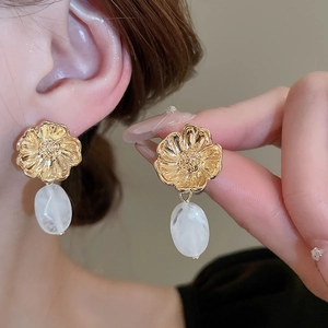 Macro detail of gold floral earrings with resin teardrop pendants and relief texture