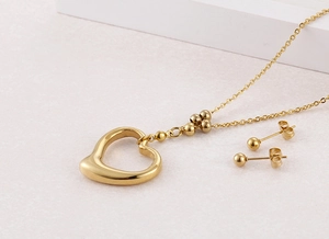 Detail view of a gold heart pendant necklace and matching ball stud earrings set