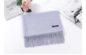 Detail of grey cashmere scarf with fringe tassels on white table with lifestyle props