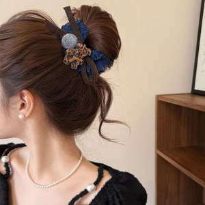 Detailed view of a dark blue and brown fabric hair clip with a leopard pattern and grey pompom