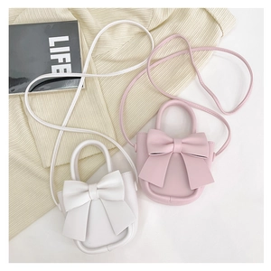 Close-up of stylish bow crossbody bags in white and pink PU leather on a beige knit