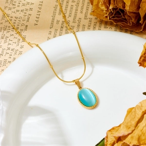 Detailed macro shot of vintage gold chain with oval turquoise pendant on white ceramic plate