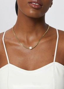 Detailed close-up of a gold Cuban chain necklace with a white baroque pearl pendant on a model