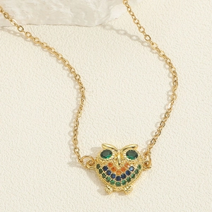 Macro detail of a golden owl pendant necklace with vibrant blue and green zircons