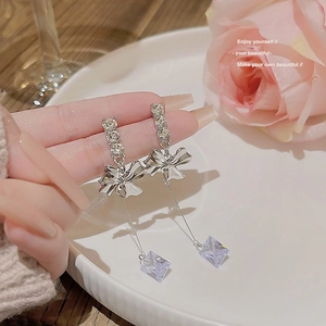 Detail of silver bow earrings with hanging square crystals and pavé rhinestones