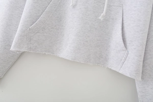 Detail of raw hem design and kangaroo pocket on light grey hooded sweatshirt for women
