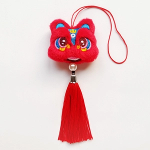 Détail d'un pendentif lion en peluche rouge avec broderie fine et longue pampille