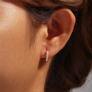 Close-up of gold hoop earring with pavé-set white zircon stones on a model's ear
