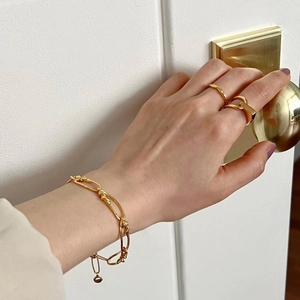 Close-up of gold chain knot bracelet and minimalist rings on hand holding a doorknob