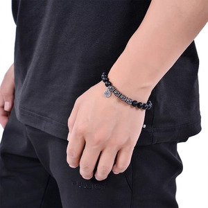Detail of matte black stone bracelet with compass charm worn on male wrist