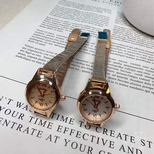 Minimalist rose gold quartz watch with mesh strap and Roman numerals on a vintage book