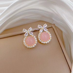 Macro view of gold bow earrings with pink gemstone and crystals on white silk