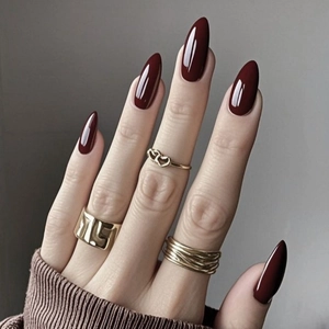 Faux ongles amande bordeaux brillant avec bagues dorées et maille marron